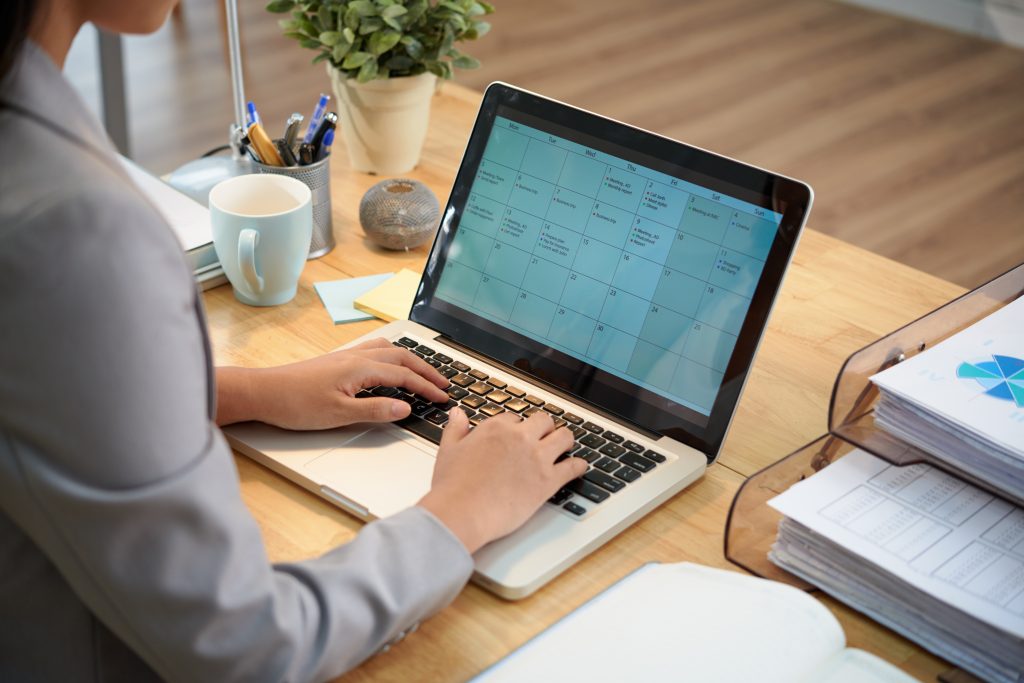 Unrecognizable businesswoman sitting desk with laptop looking calendar